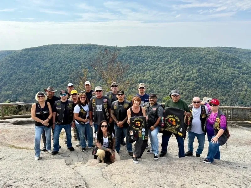Group of bikers posing on a scenic cliff with forested hills in the background.